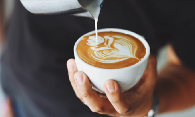 En kaffekopp i sentrum, mens det helles melk opp i koppen. IMG