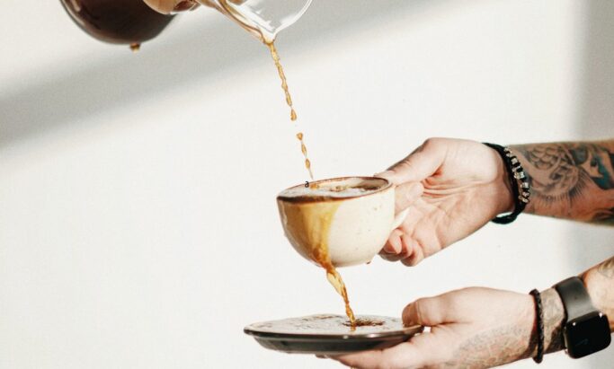 Helle kaffe fra kaffekanne ned i kaffekopp som renner over