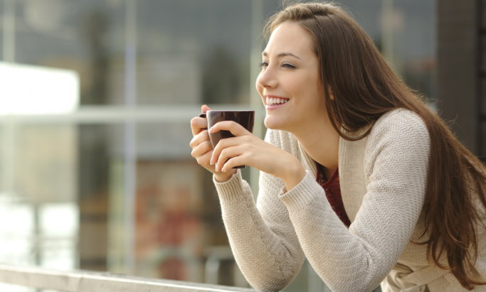 En ung kvinner smiler med en kopp kaffe