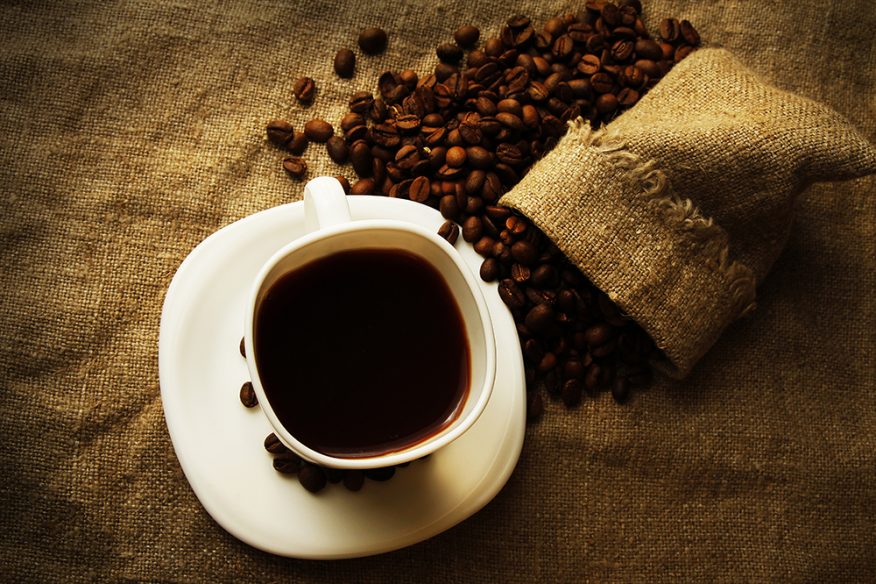 Hvit kopp med sort kaffe og kaffebønner spredt på et bord